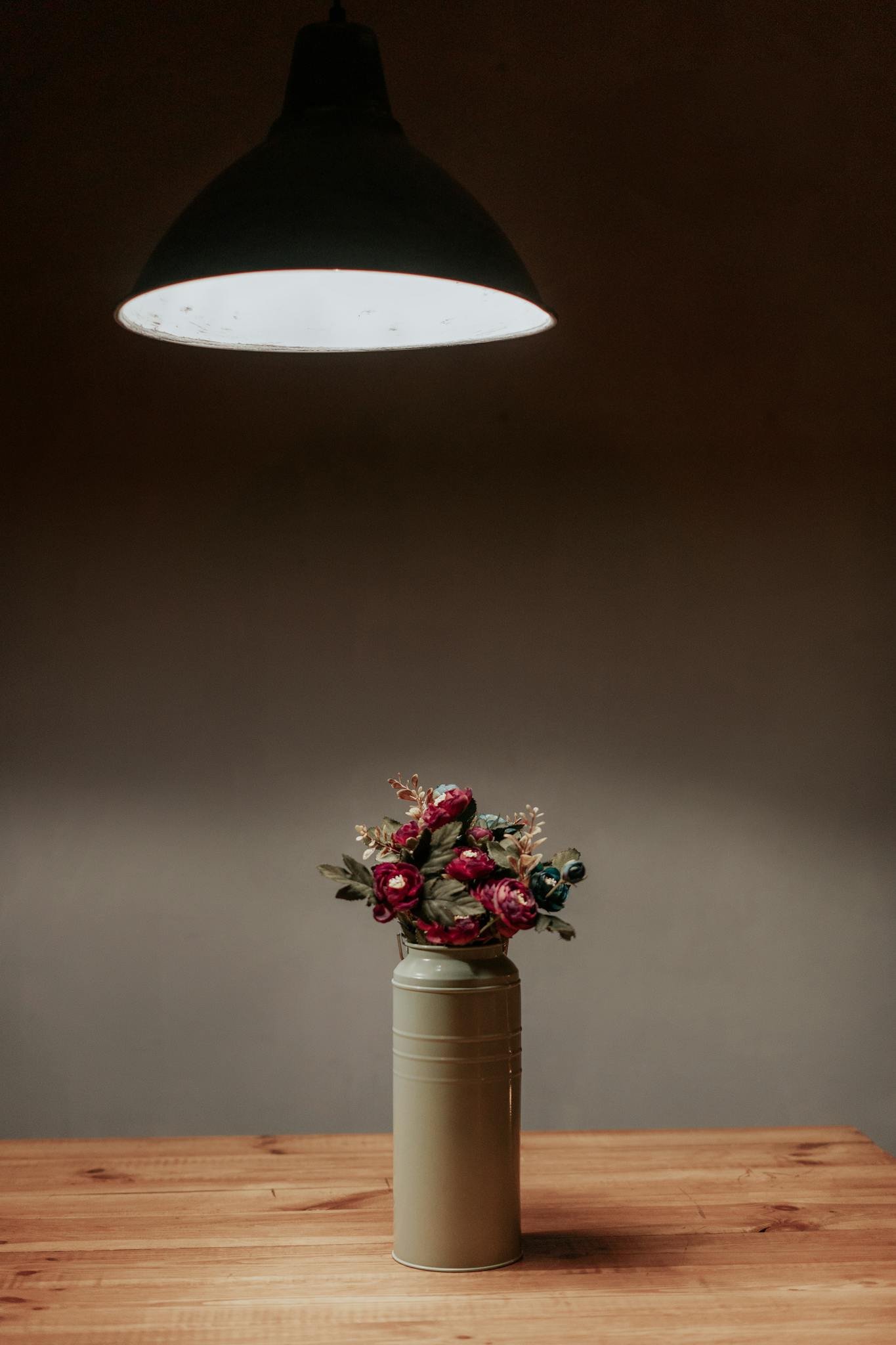 Vintage floral arrangement in a vase under a pendant light on a wooden table.